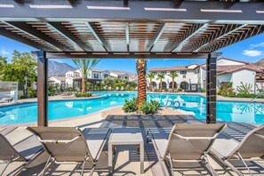 A pool area with lounge chairs, a pergola, and a view of residential buildings. - Furnished Patio + Putting Green: La Quinta Home (La Quinta)
