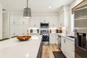 A modern kitchen with white cabinetry, a large island, stainless steel appliances, and a hanging light fixture. - Furnished Patio + Putting Green: La Quinta Home (La Quinta)