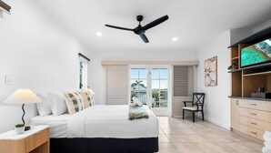A bedroom with a bed, bedside table, lamp, ceiling fan, and a view of the outdoors. - Cullen Bay Retreat | Pool, Balcony & Marina Stroll (Larrakeyah)
