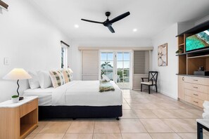 Ein Schlafzimmer mit Bett, Nachttisch, Lampe, Deckenventilator und Blick ins Freie.