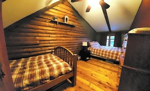 A log cabin room with two beds, a small table, and a window.