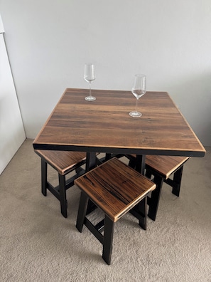 A square wooden table with four matching benches, two wine glasses on the table. - Golden Mile Beachside (Manly)