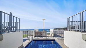 Une piscine sur le toit offrant une vue dégagée sur l’océan, entourée d’une balustrade blanche et agrémentée d’un grand poteau au centre.