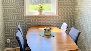 A dining area with a wooden table, four chairs, a vase with flowers, and a window with a view of a green field and trees. - 4 Star Holiday Home in Bodafors (Bodafors)