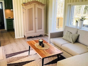 A living room with a sofa, a wooden coffee table with a placemat, a cabinet, and a view of the outdoors through a window.