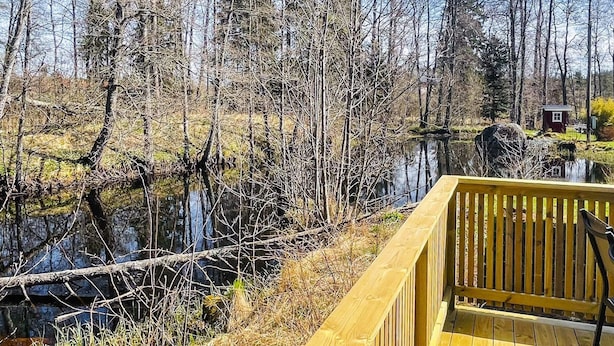 A wooden deck overlooking a pond with trees and a small cabin in the background. - 4 Star Holiday Home in Bodafors (Bodafors)