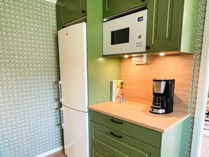 Una kitchenette compacta con refrigerador, microondas, cafetera y un pequeño armario con papel tapiz estampado.