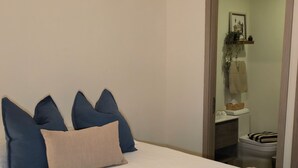 A bedroom with a bed, pillows, a bedside table, a mirror, and a door leading to a bathroom. - Cozy 1-bedroom condo with AC in welcoming Punta Cana (Punta Cana)