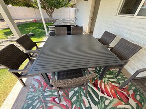 Un patio con una mesa y sillas, un tapete estampado y un árbol al fondo.