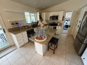 Una cocina moderna con armarios blancos, una isla central con dispensador de agua y un refrigerador de acero inoxidable.