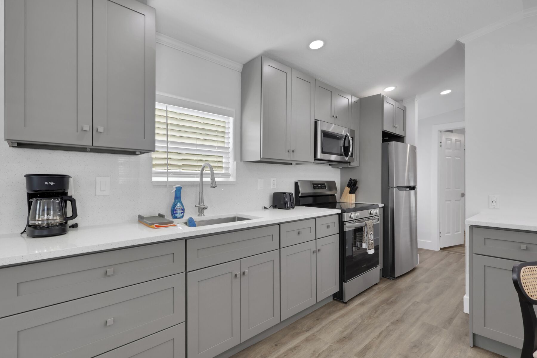 A modern kitchen with grey cabinets, a stainless steel refrigerator, a microwave, and a coffee maker.