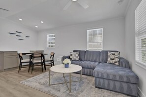 A modern living room with a grey sofa, a round coffee table, and a dining area with a small table and chairs.