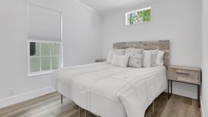 A bedroom with a bed, a nightstand, a window with blinds, and a small picture frame on the wall. - Renovated Naples Retreat- Resort Pool & Game Room (Naples)
