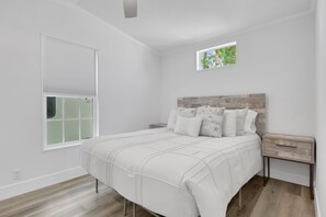 A bedroom with a bed, a nightstand, a window with blinds, and a small picture frame on the wall. - Renovated Naples Retreat- Resort Pool & Game Room (Naples)