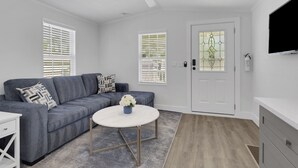 A modern living room with a grey sofa, a round coffee table, and a ceiling fan. - Renovated Naples Retreat- Resort Pool & Game Room (Naples)