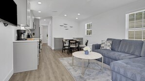 A modern living room with a gray sofa, a coffee table, and a dining area with a table and chairs. - Renovated Naples Retreat- Resort Pool & Game Room (Naples)