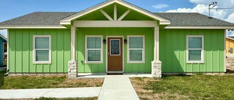 A single-story house with a green facade, a front porch, and a front door.