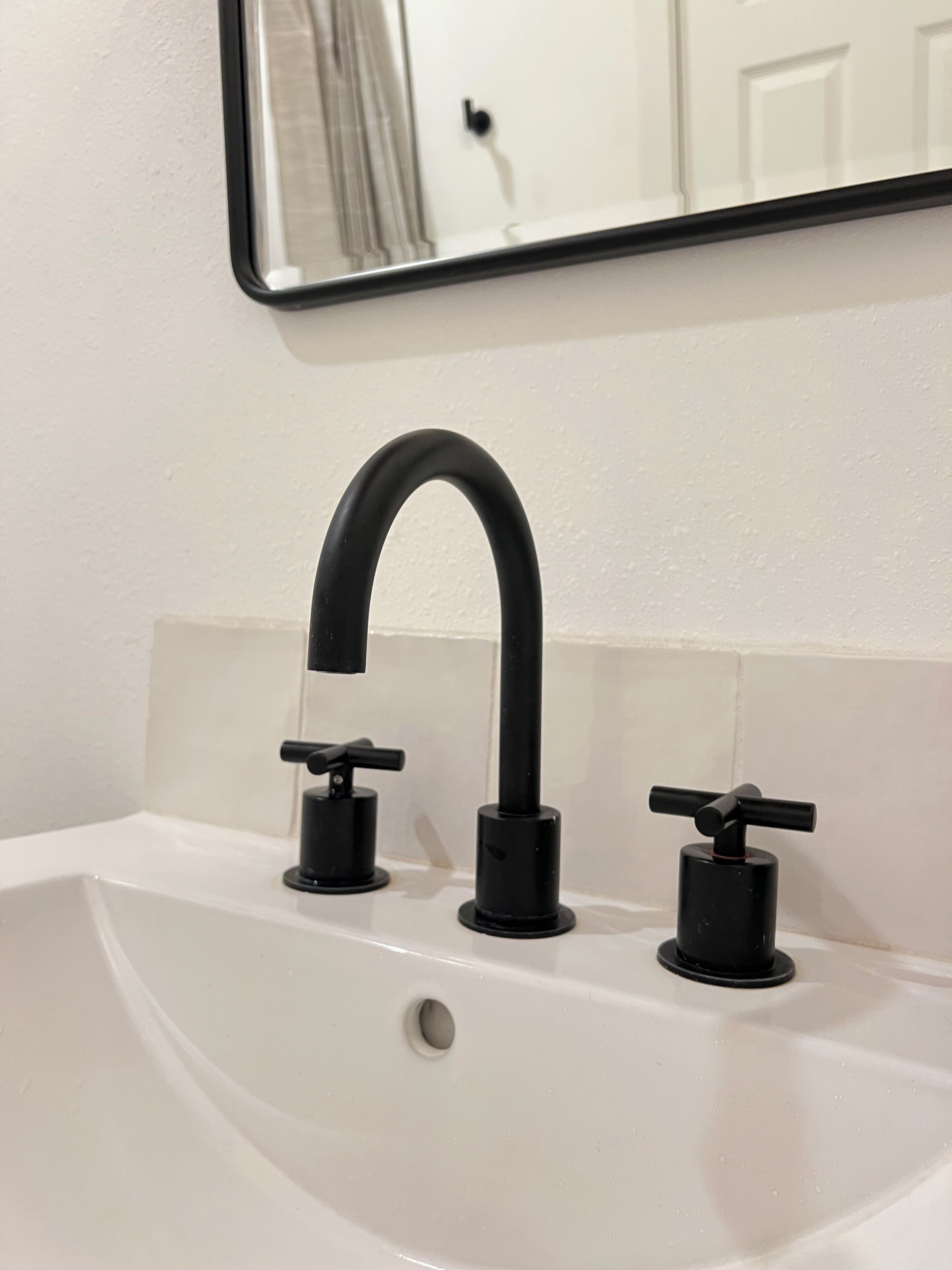 Un lavabo blanc dans une salle de bain, avec un robinet noir et un miroir au-dessus.