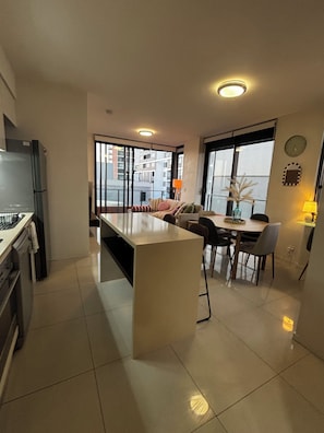 A modern kitchen with a dining area, large windows, and a view of the city. - Listen to & watch the waves, swim, surf, see dolphins & whales! (Newcastle)