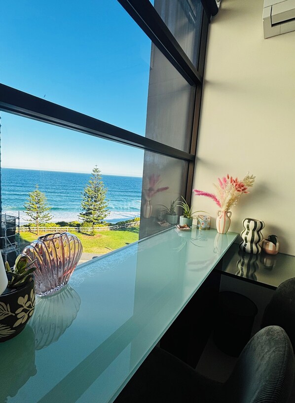 A modern room with a large window overlooking the ocean, a glass table, and various decorative items.
