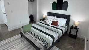 Une chambre moderne avec un grand lit, une table de chevet avec une lampe, une œuvre d’art accrochée au mur et un tapis à motifs.