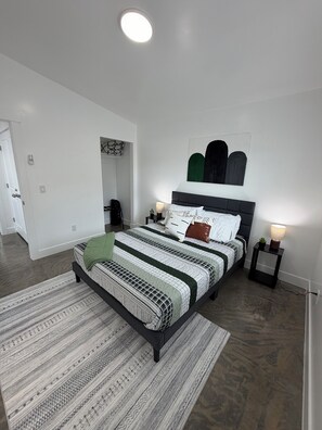 Un dormitorio moderno con una cama grande, una mesita de noche con lámpara, una obra de arte en la pared y una alfombra estampada.