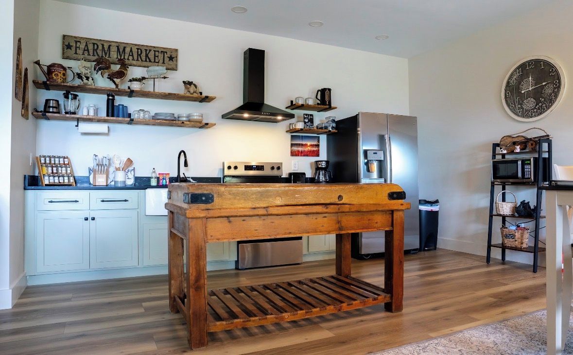 Eine Küche mit einem Holztisch in der Mitte, weißen Schränken, einem Edelstahlkühlschrank und einer Uhr an der Wand.