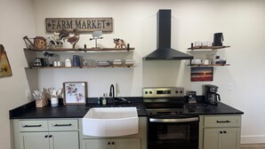 Een keuken met een kookplaat, oven, spoelbak en decoratieve spullen op planken.