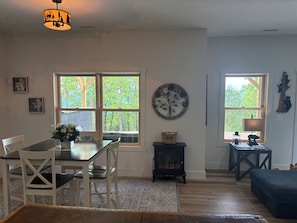 Una sala de estar con mesa de comedor, sillas, chimenea y ventanas amplias con vista a árboles.