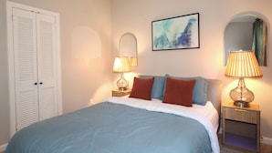 Una camera da letto con un letto, due lampade sui comodini, uno specchio a parete e una porta.