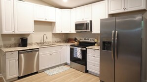 Una cucina con mobili bianchi, elettrodomestici in acciaio inossidabile, lavastoviglie e forno a microonde.