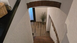 A staircase with a brick wall on one side and a white wall on the other, leading to a room with a window and a plant. - Duplex Apartment (Bologna)