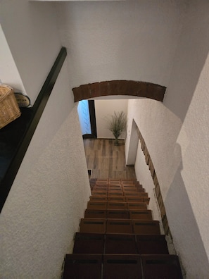 A staircase with a brick wall on one side and a white wall on the other, leading to a room with a window and a plant. - Duplex Apartment (Bologna)