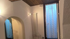 A room with a wooden floor, white walls, a radiator, a chair, and a window with curtains. - Duplex Apartment (Bologna)