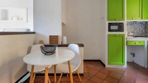 A compact kitchen with green cabinets, a microwave, and a white table with two chairs. - Duplex Apartment (Bologna)