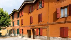 A two-story building with red shutters, a tiled ground floor, and a stone base. - Duplex Apartment (Bologna)