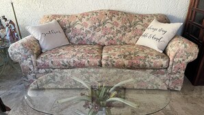 Un divano con motivo floreale, due cuscini, un tavolino in vetro e un vaso con fiori.