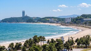 A coastal beach with a sandy shore, a clear blue sea, and a backdrop of buildings and hills. - Yangyang J Ocean View (Yangyang)
