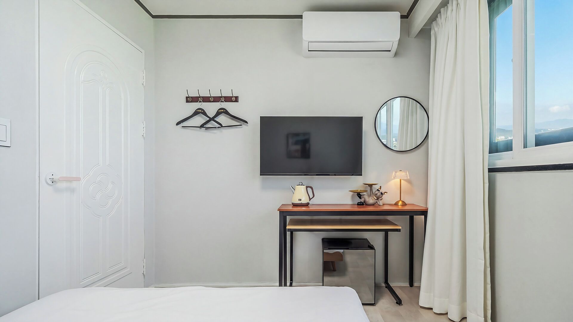 Ein Hotelzimmer mit Bett, Schreibtisch mit Wasserkocher und Lampe, Fernseher, Kleiderständer und Klimaanlage.