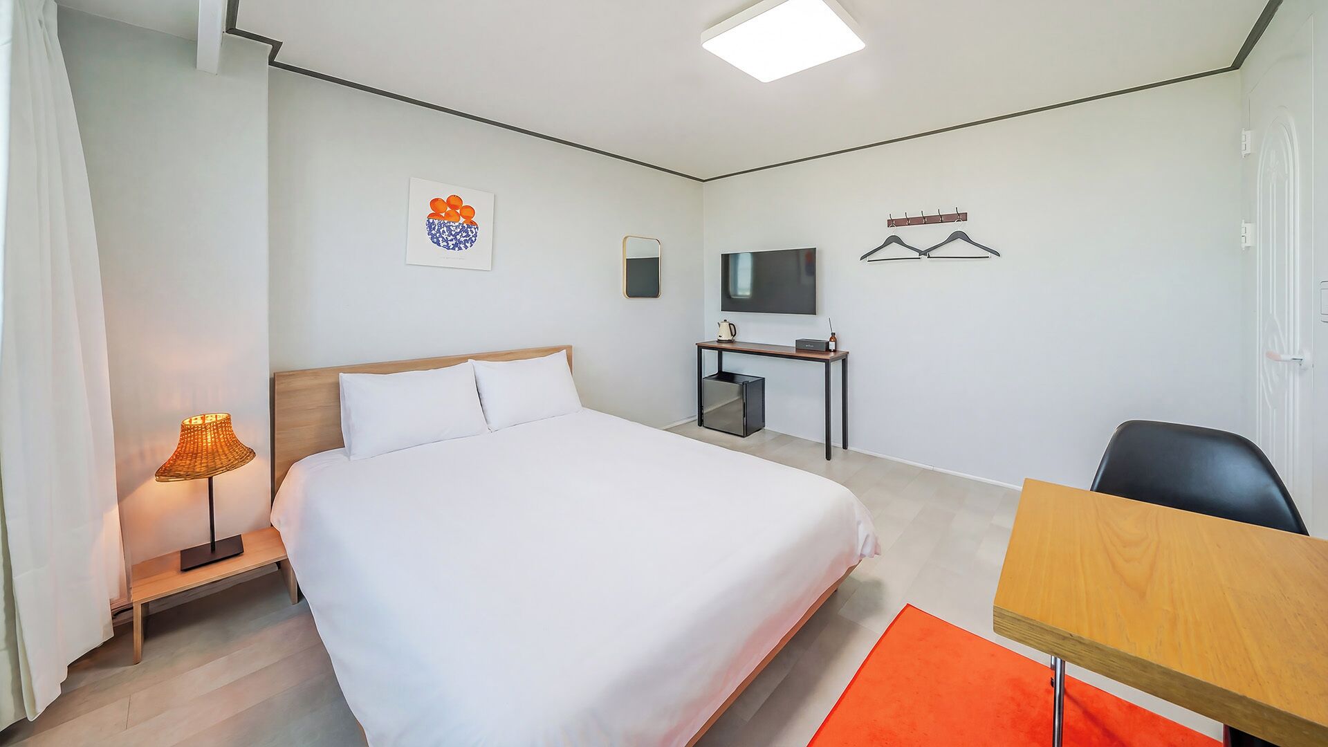 A hotel room with a bed, a desk, a chair, a TV, and a wall-mounted coat rack.
