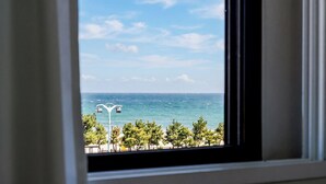 Vista a través de una ventana de una zona costera con farol, árboles y el océano.
