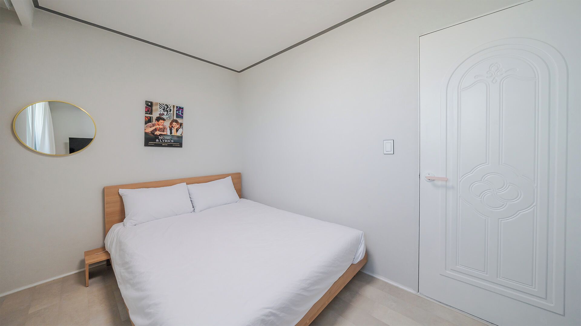 Un dormitorio con una cama, un espejo redondo, un cartel y una puerta.