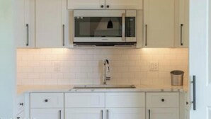 Uma cozinha com armários brancos, micro-ondas, pia e lixeira.