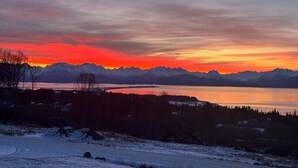 Paisagem nevada com uma cordilheira e um corpo d'água ao pôr do sol.