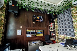 A bar area with wooden paneling, a television, shelves with beverages, and a seating area.