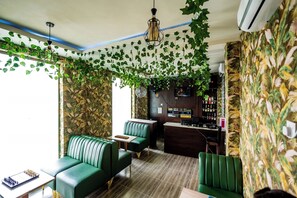 A room with a green sofa, a small table with a chessboard, a bar area with a wooden counter, and a ceiling fan. - RJ Hotel Port Harcourt (Port Harcourt)