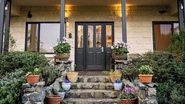 Une maison à deux étages avec une porte d’entrée sombre, un balcon et un escalier en pierre menant à l’entrée.