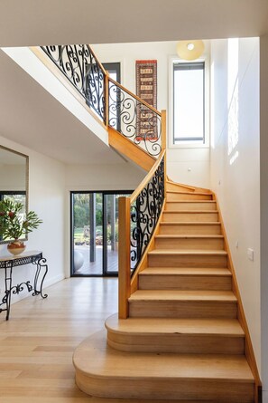 A wooden staircase with black iron railings, a potted plant, and a large window. - Premium coastal homestead. Gardens, farmland, adventure. Sleeps 8. Pet friendly. (Waratah Bay)