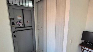 Huone, jossa on harmaa ovi, pieni työpöytä, jossa on tietokone, ja laatoitettu lattia.