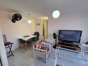 Un espace de vie compact comprenant un coin repas, un téléviseur et un lit avec une literie aux couleurs vives.